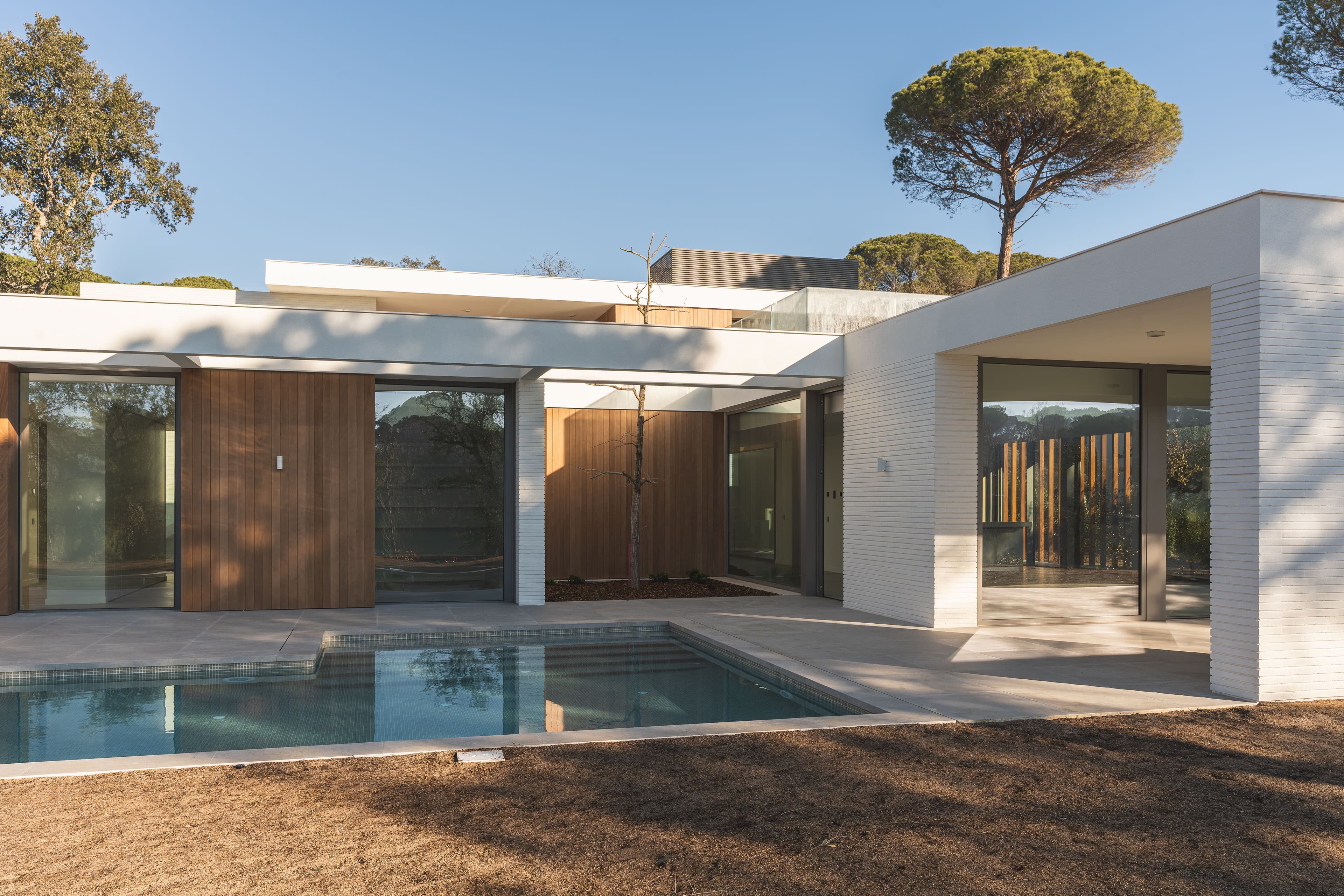 White and wooden luxury house with private pool in a high-end urbanization seen from the outside